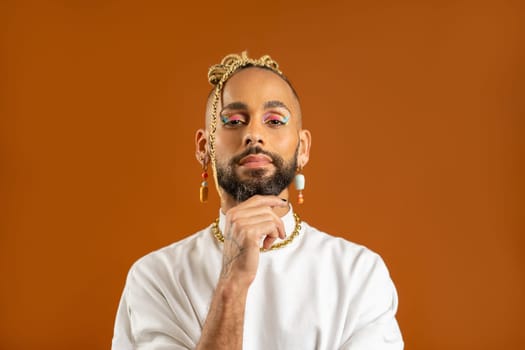 Confident bearded black gay man with bright makeup standing isolated on orange background, dressed white. Exudes sense of pride and individuality. Diversity power of personal style