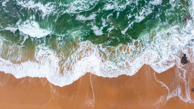 Drone view of beautiful seamless footage while turquiose sea waves breaking on sandy coastline. Aerial shot of golden beach meeting deep blue ocean water and foamy waves