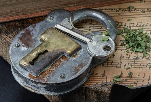 Bangkok,Thai - Mar 17, 2023 : The Key and the Vintage Iron Padlock with chopped cannabis leaves on the old vintage music note with the old wooden plank background.