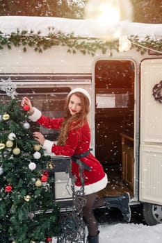 Young woman in santa costume decorates the Christmas tree at winter campsite getting ready for the new year. New year celebration concept