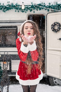 Young woman in santa costume decorates the Christmas tree at winter campsite getting ready for the new year. New year celebration concept