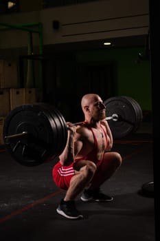 Shirtless caucasian man squats with a barbell in the gym