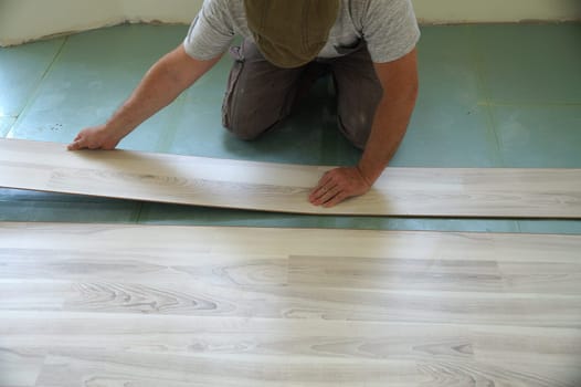 Worker laying laminate flooring in a room.