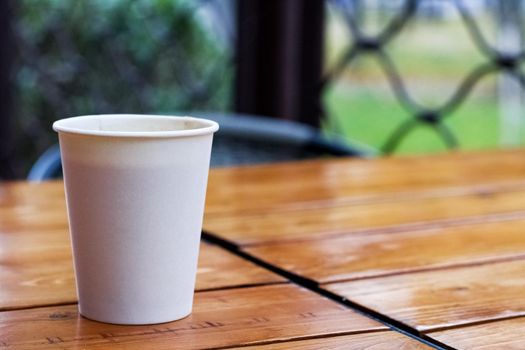 White paper cup with coffee on a wooden table, copy space