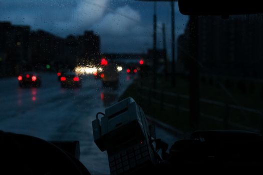 Car front window with raindrops and road with cars at night close up