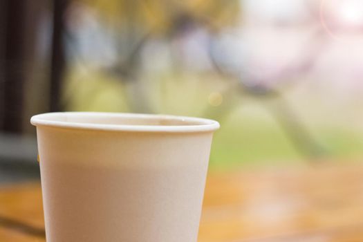 White paper cup with coffee on a wooden table, copy space