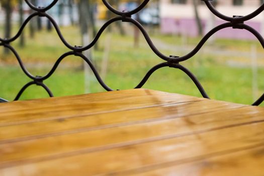 Wooden table and yellow autumn trees behind a metal mesh