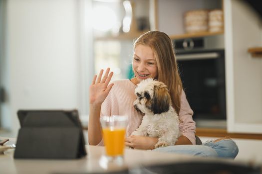 Shot of a beautiful teenage girl sitting with her cute dog and making a video call on a digital tablet while having leisure time at her home during covid-19 pandemic.