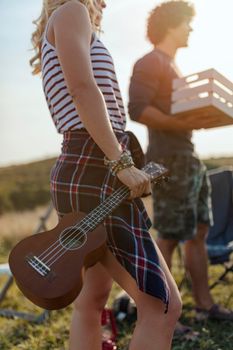 An attractive young woman holds a ukulele and preparing to play music to her friends while their having fun outside their tent at a festival.