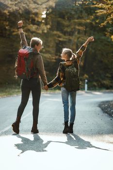 Rearview shot of a teen girl and her mom walking together through the forest in autumn.