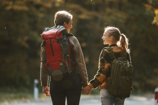 Rearview shot of a teen girl and her mom walking together through the forest in autumn.