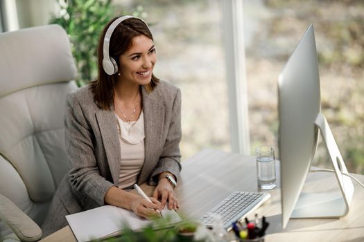 A smiling business woman with headphones using a computer to have a web conference at home office.