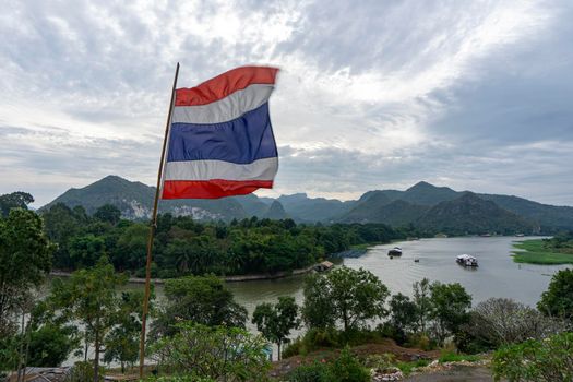 Thai flag blown from the wind, the background is the view of the River Kwai and the mountains of Kanchanaburi, Thailand