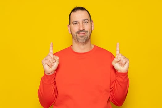 Handsome hispanic man with a beard wearing a red sweater pointing up with his fingers, isolated over yellow background.