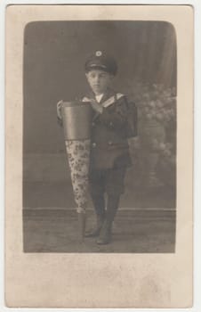 WALDENBURG, GERMANY - CIRCA 1920s: Vintage photo shows little boy with a School Cone - Tute a big cardboard cone with toys, chocolate, candies, given the first day of school. Retro black and white studio photography. Circa 1920s.