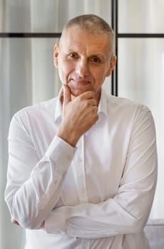 Portrait of a smiling businessman in a white shirt who is posing holding his hand to his face. Vertical frame.