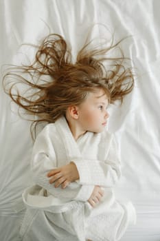 A girl in a white coat lies in bed, looks away. View from above.