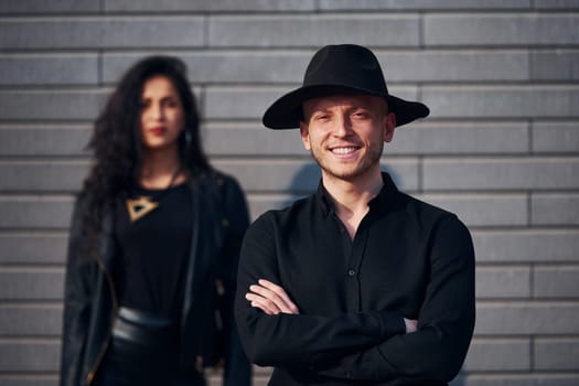 Beautiful couple in black clothes together against wall outdoors.