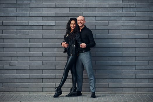 Beautiful couple in black clothes dancing together against wall outdoors.