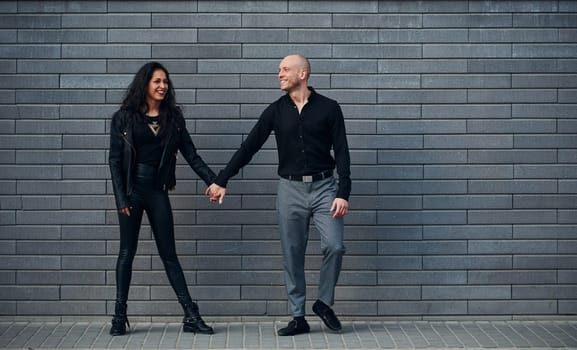 Beautiful couple in black clothes together against wall outdoors.