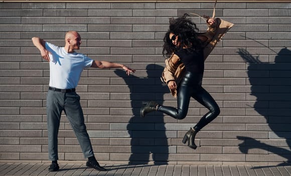 Beautiful couple in black clothes dancing together against wall outdoors.