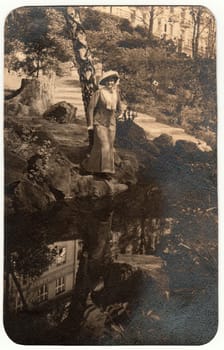 THE CZECHOSLOVAK REPUBLIC - CIRCA 1930s: Vintage photo shows woman wears an elegant dress and feather hat. The woman poses outdoors at the bank of river. Retro black and white photography. Circa 1960s.