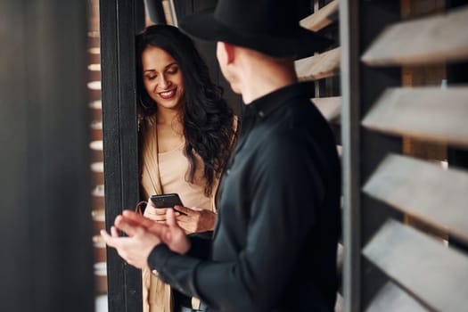 Woman with black curly hair and her man standing together near wooden windows.