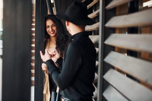 Woman with black curly hair and her man standing together near wooden windows.