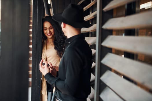 Woman with black curly hair and her man standing together near wooden windows.