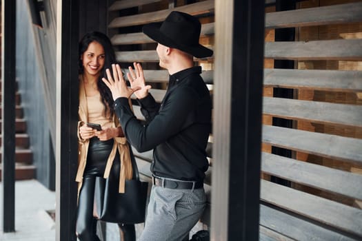 Woman with black curly hair and her man standing together near wooden windows.