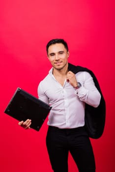 Image of young cheerful businessman holding and using laptop isolated over red background