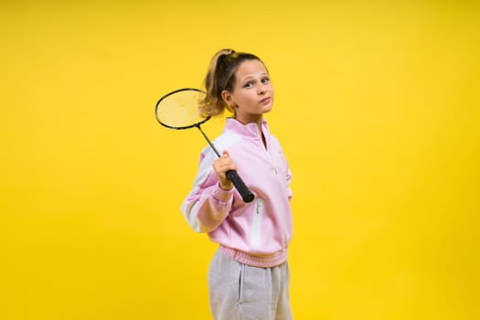 Full length studio photo of ten year old girl holding a badminton racket and isolated on yellow.