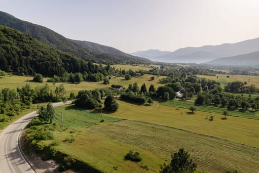 Top view of hilly local green autumn forest and mountain road. Landscape of green forest and village.