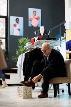 Senior customer trying elegant shoes in modern boutique, shopping for fashionable clothes and accessories. Elderly stylish man buying new collection in clothing store. Fashion concept