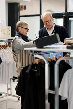 Elderly couple looking at blue stylish shirt analyzing fabric in clothing store, looking at new fashion collection. Caucasian people shopping for formal wear, buying fashionable merchandise