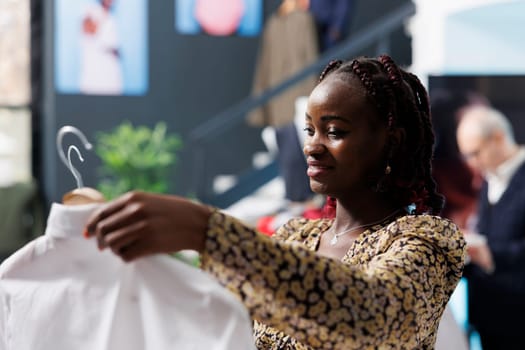 Pregnant client checking trendy white shirt in modern boutique, shopping for fashionable pregnancy clothes. African american woman buying stylish formal wear in clothing store. Fashion concept