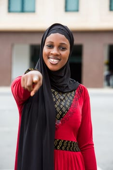 young woman standing outdoors with veil pointing at something with a smile.