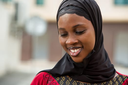 young woman standing outdoors with veil smiling to smile with head down.