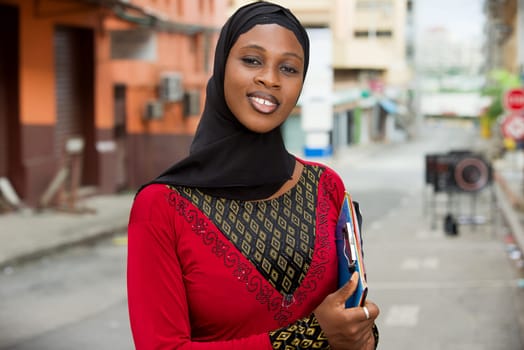 young muslim female student standing outdoors looking at camera smiling.