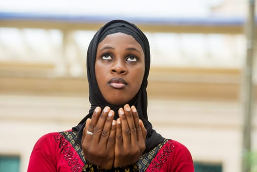 young muslim woman standing outdoors praying.
