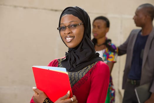 young muslim woman standing in eyeglasses outdoors looking at camera smiling.