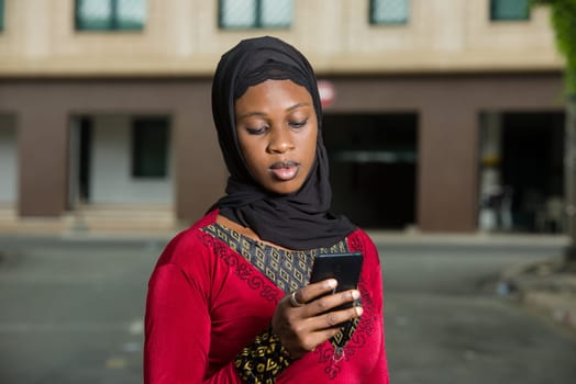 young muslim woman standing outdoors looking at cell phone.