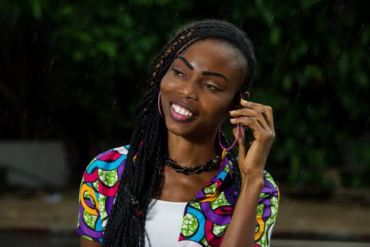 African girl standing under a fine rain communicating smiling.