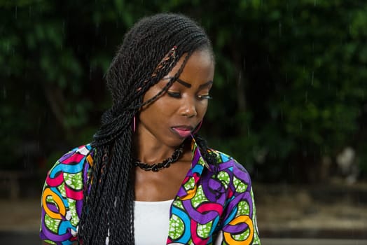 young african girl standing under a light rain staring at something.