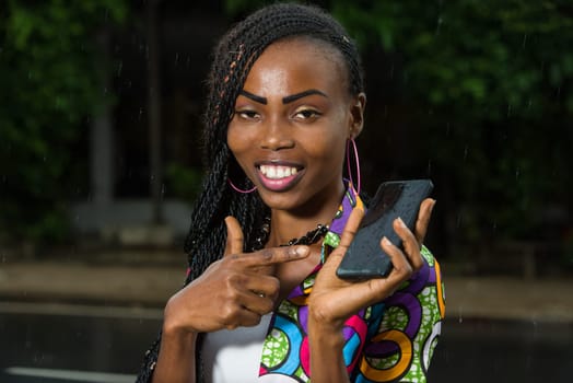 young girl under a light rain show mobile phone smiling.