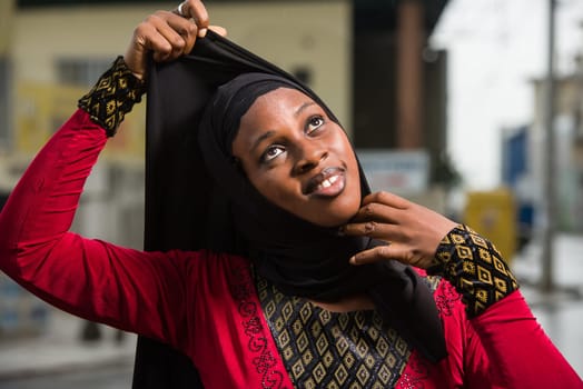 young muslim woman standing outdoors adjusting her veil while smiling.