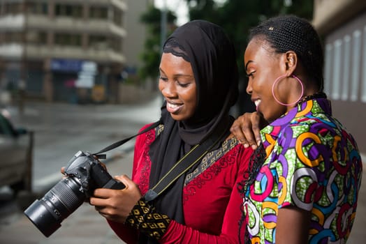 Young women standing outdoors look at camera smiling.