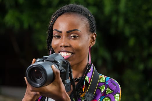 young woman standing in full with camera and looking in front of her smiling.
