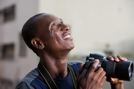 young man standing outdoors with camera staring up at smiling.