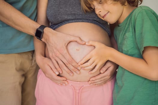 Pregnant Woman, father and first kid child holding hands in a heart shape on her baby bump. Pregnant Belly with fingers Heart symbol.